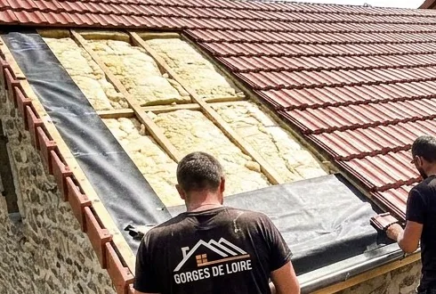 Isolation des combles en cours à Saint-Just-Saint-Rambert : laine posée entre les chevrons d'un versant ouvert, à côté des tuiles mécaniques déjà reposées